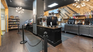 Interior moderno de una cafetería con pared de madera en espiga, una barra central con máquinas de café y una zona de bar con estantes llenos de bebidas.