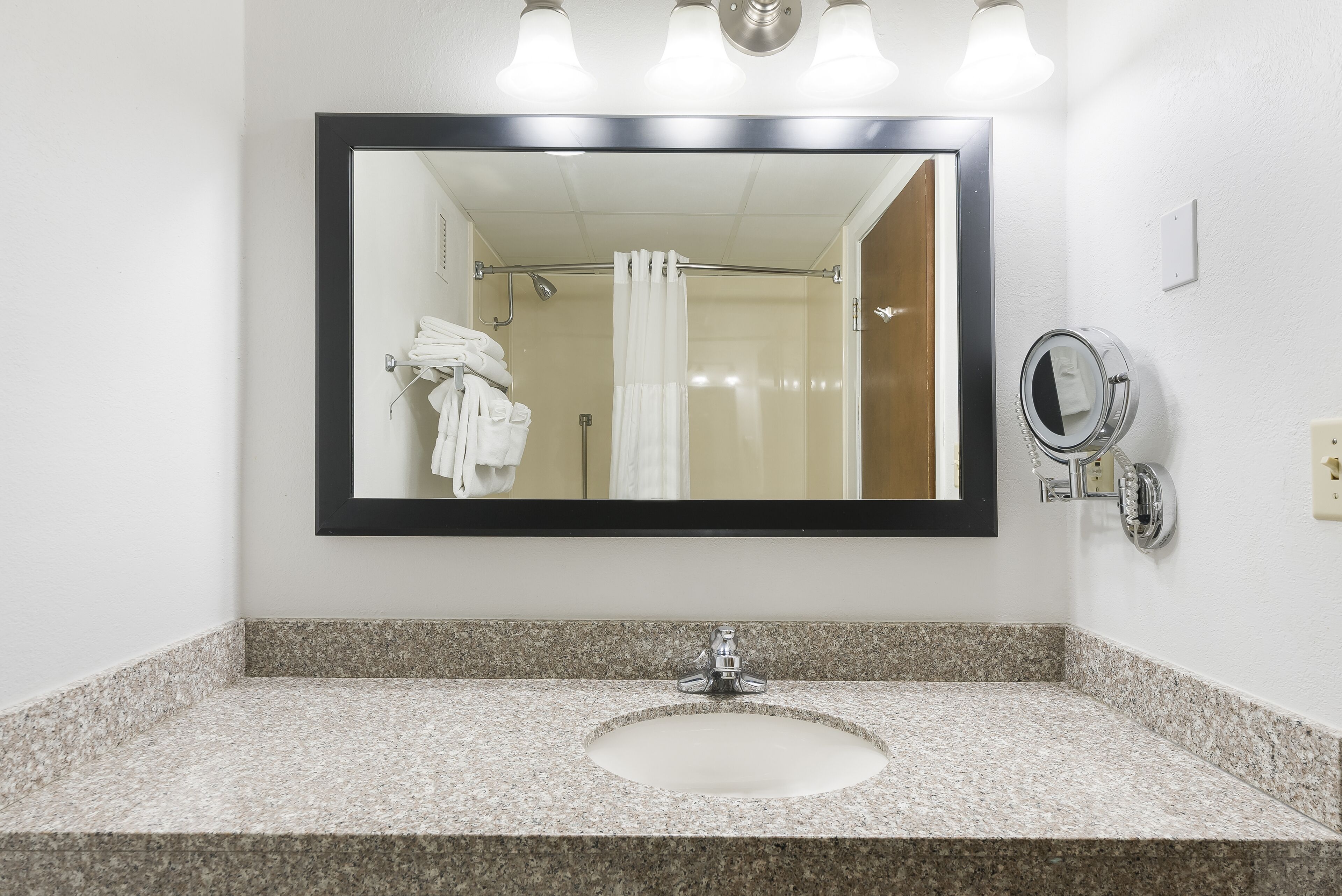 A bathroom with a granite countertop, a sink, a mirror, and a shower curtain.