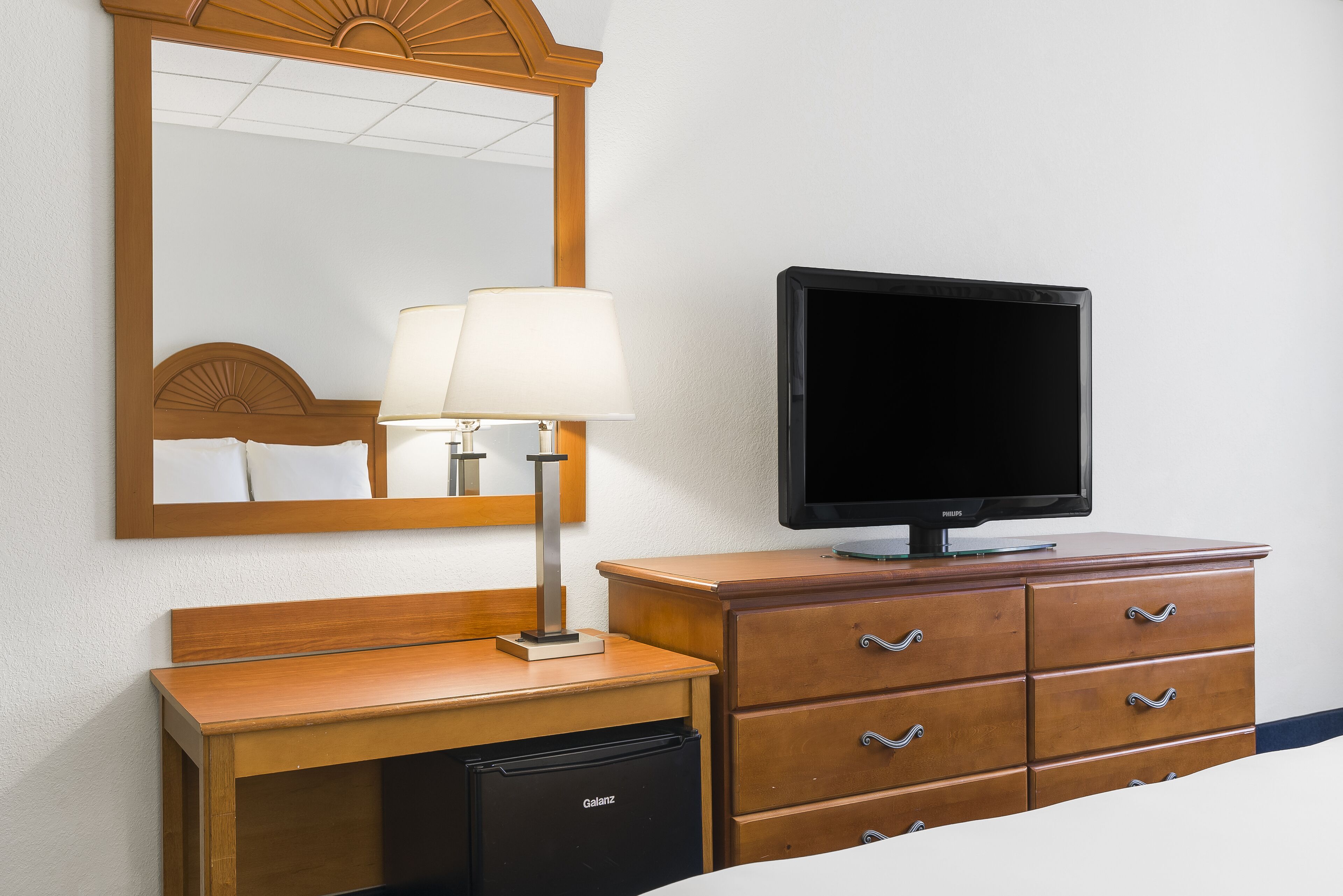 Una habitación de hotel con un escritorio de madera, un televisor, una lámpara y un espejo.