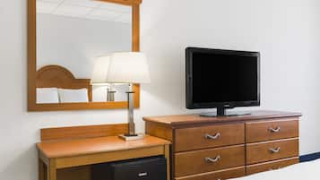 Una habitación de hotel con un escritorio de madera, un televisor, una lámpara y un espejo.