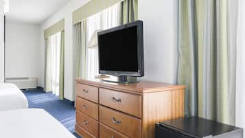 Une chambre d’hôtel avec un lit, une commode en bois avec des tiroirs, un téléviseur posé sur le dessus, un réfrigérateur noir et une fenêtre avec des rideaux à rayures.
