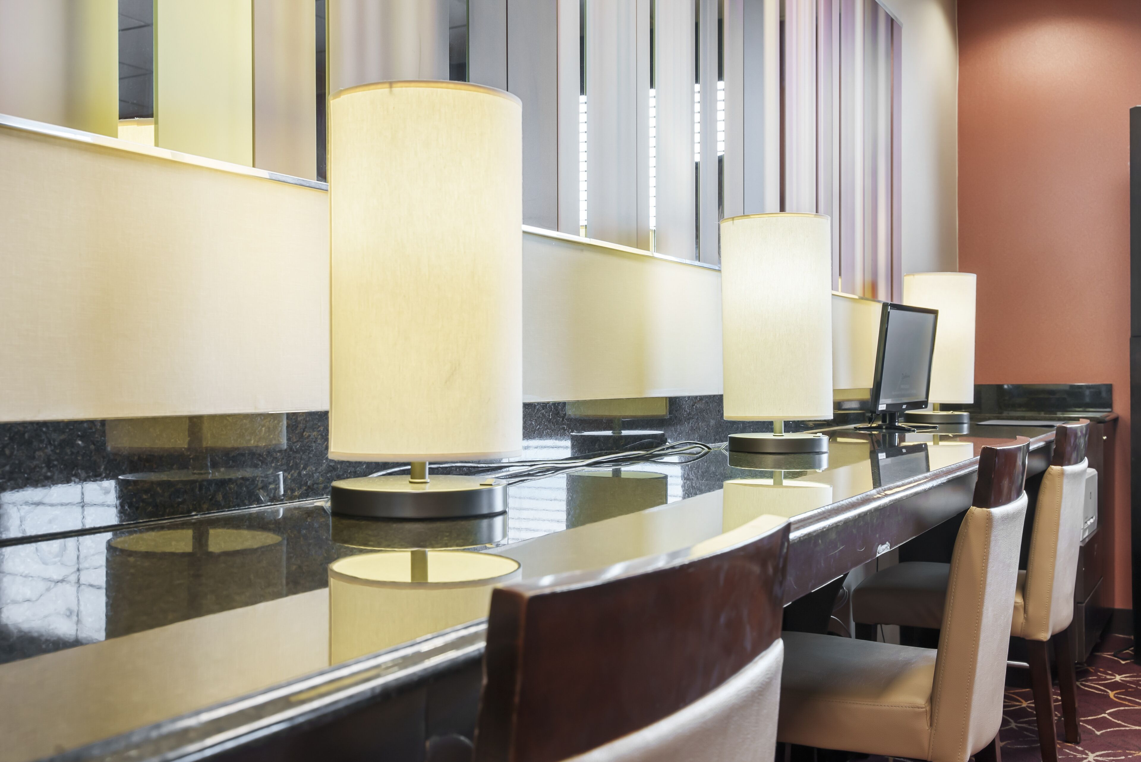 A hotel reception area with a marble counter, multiple chairs, and a large mirror reflecting the interior.