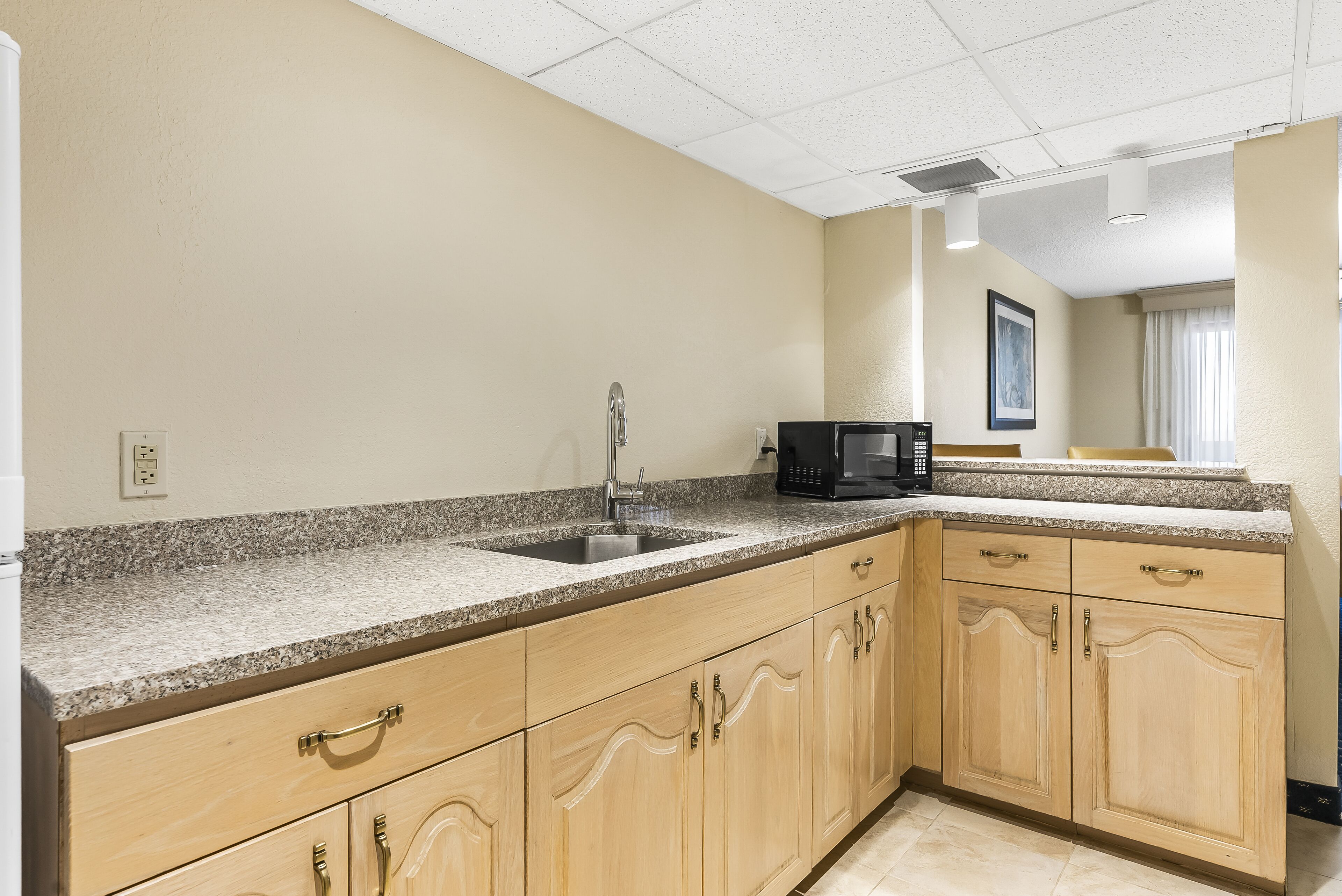 A kitchen with granite countertops, wooden cabinets, a stainless steel sink, a black coffee maker, and a window with curtains.