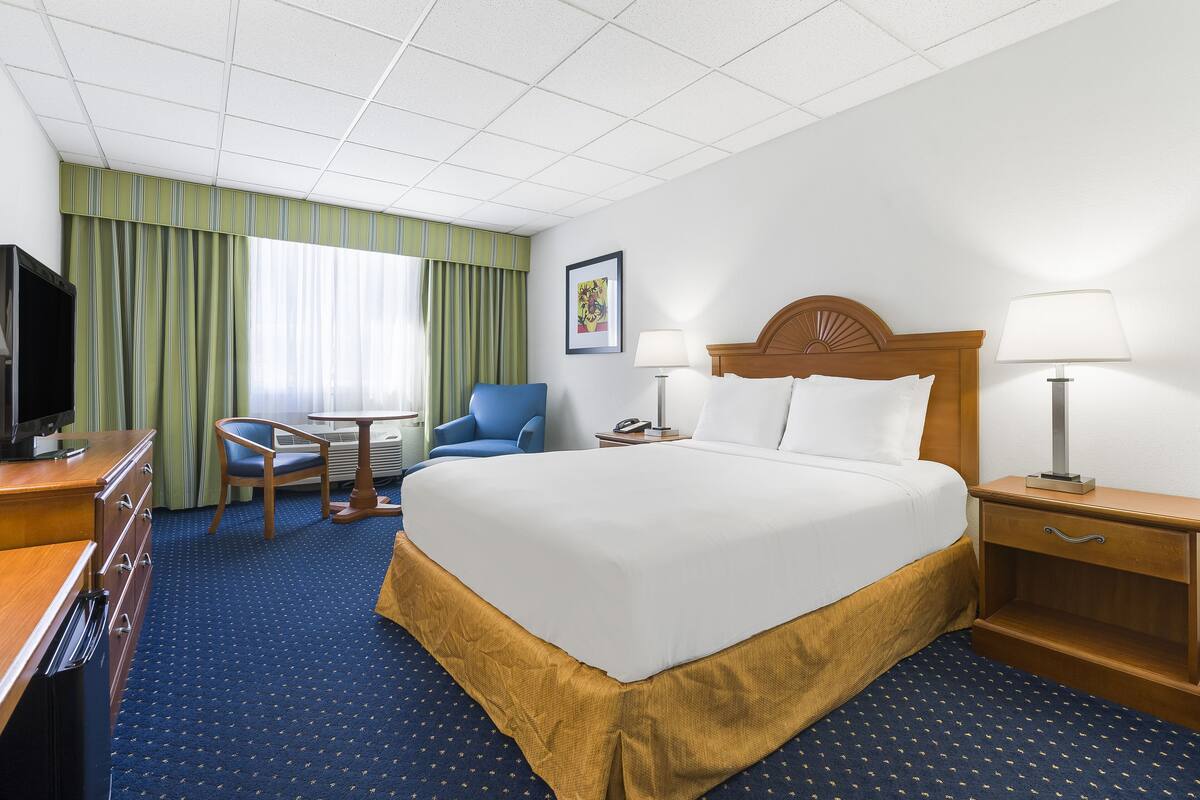 Quarto de hotel com uma cama grande, uma escrivaninha com cadeira, televisão e janela com cortinas.