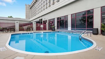 Una piscina con una cerca roja, un área de descanso cubierta y un edificio con grandes ventanales al fondo.