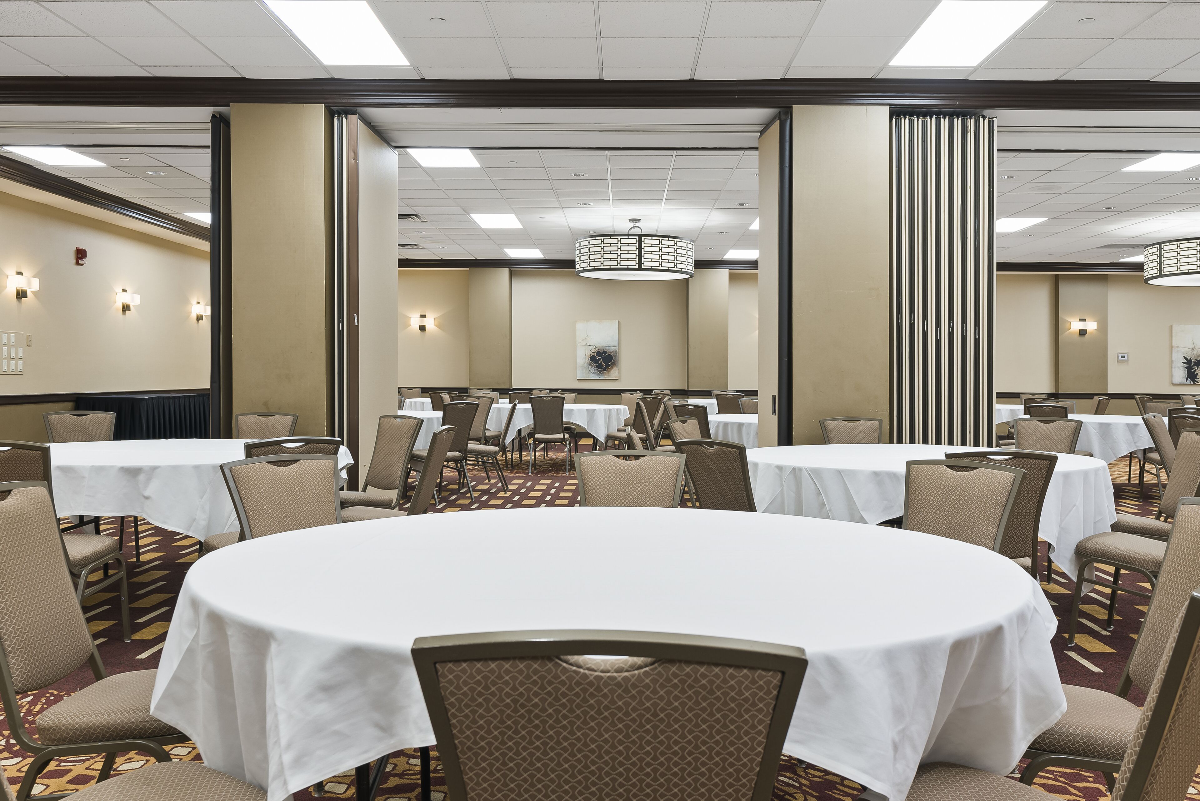 Une salle de conférence avec des tables rondes, des chaises beiges et un tapis à motifs.