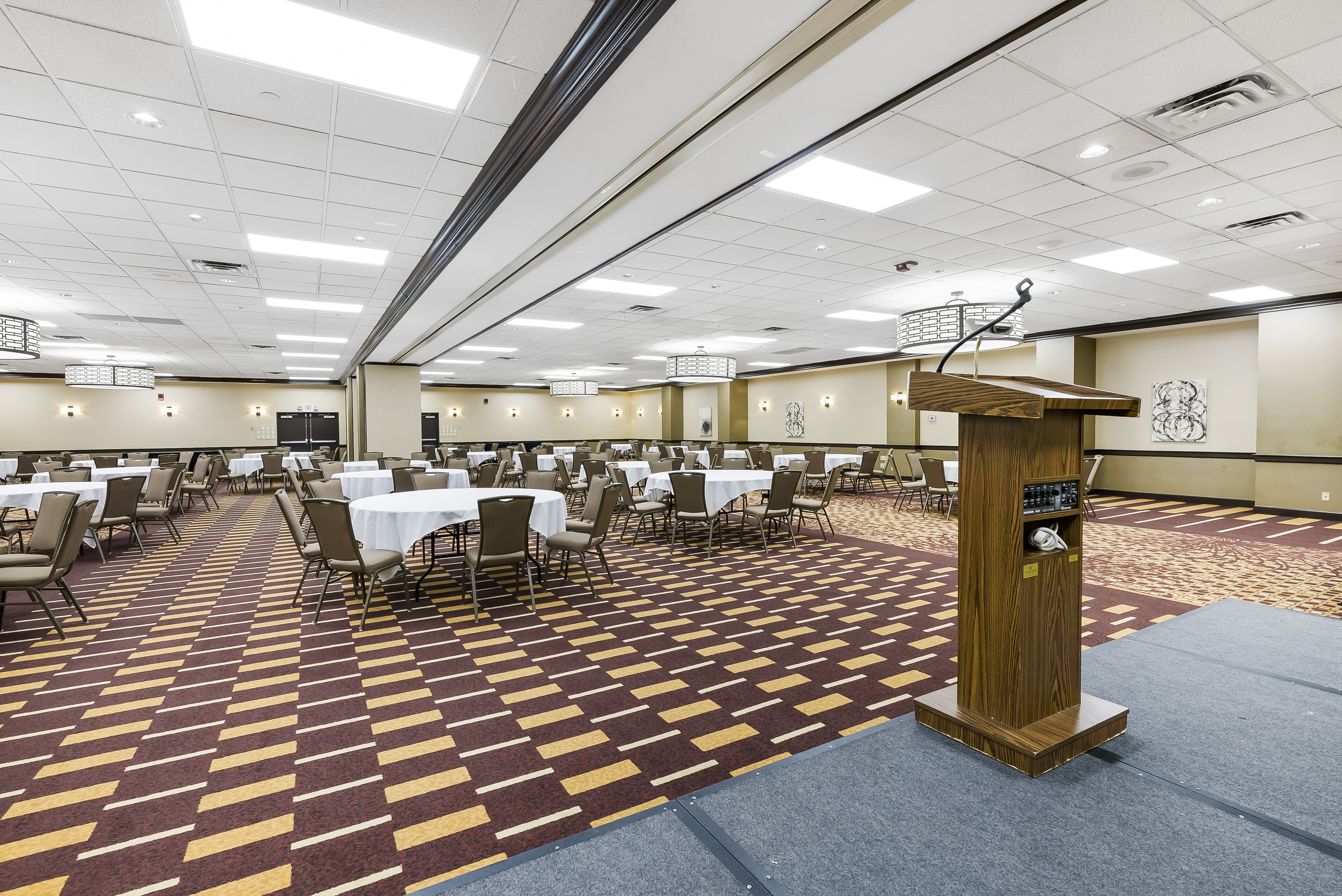 A large conference room with multiple tables and chairs, a podium, and a patterned carpet.