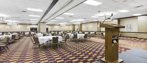 A large conference room with multiple tables and chairs, a podium, and a patterned carpet.