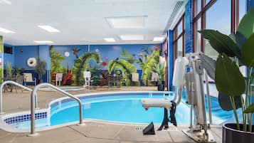 A swimming pool with a mural of tropical plants and birds on the wall, surrounded by lounge chairs and a poolside table.