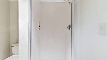 Un espacio de ducha pequeño y cerrado, con un inodoro a la izquierda.