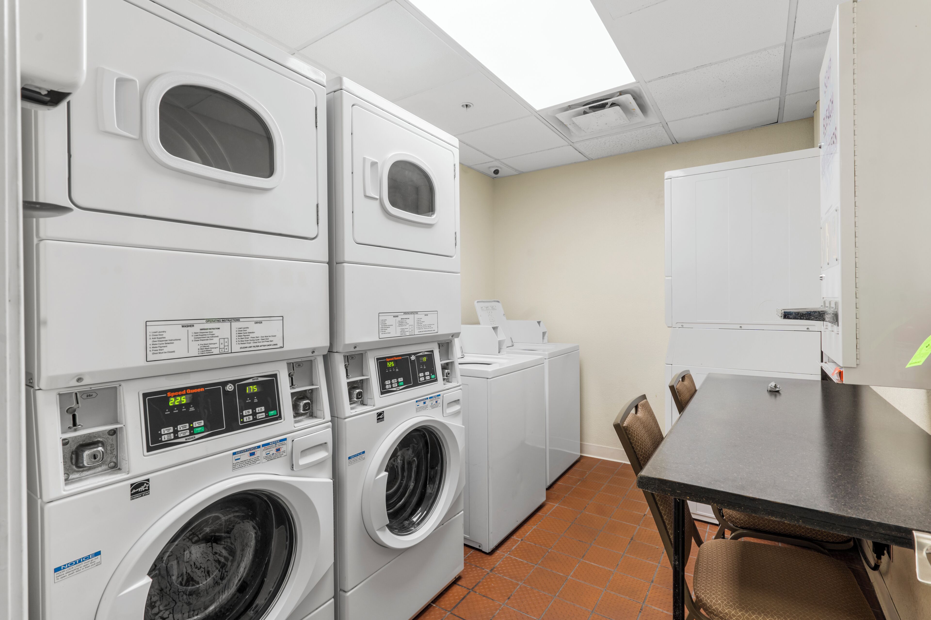A laundry room with stacked washers and dryers, a table, chairs, and a whiteboard on the wall.