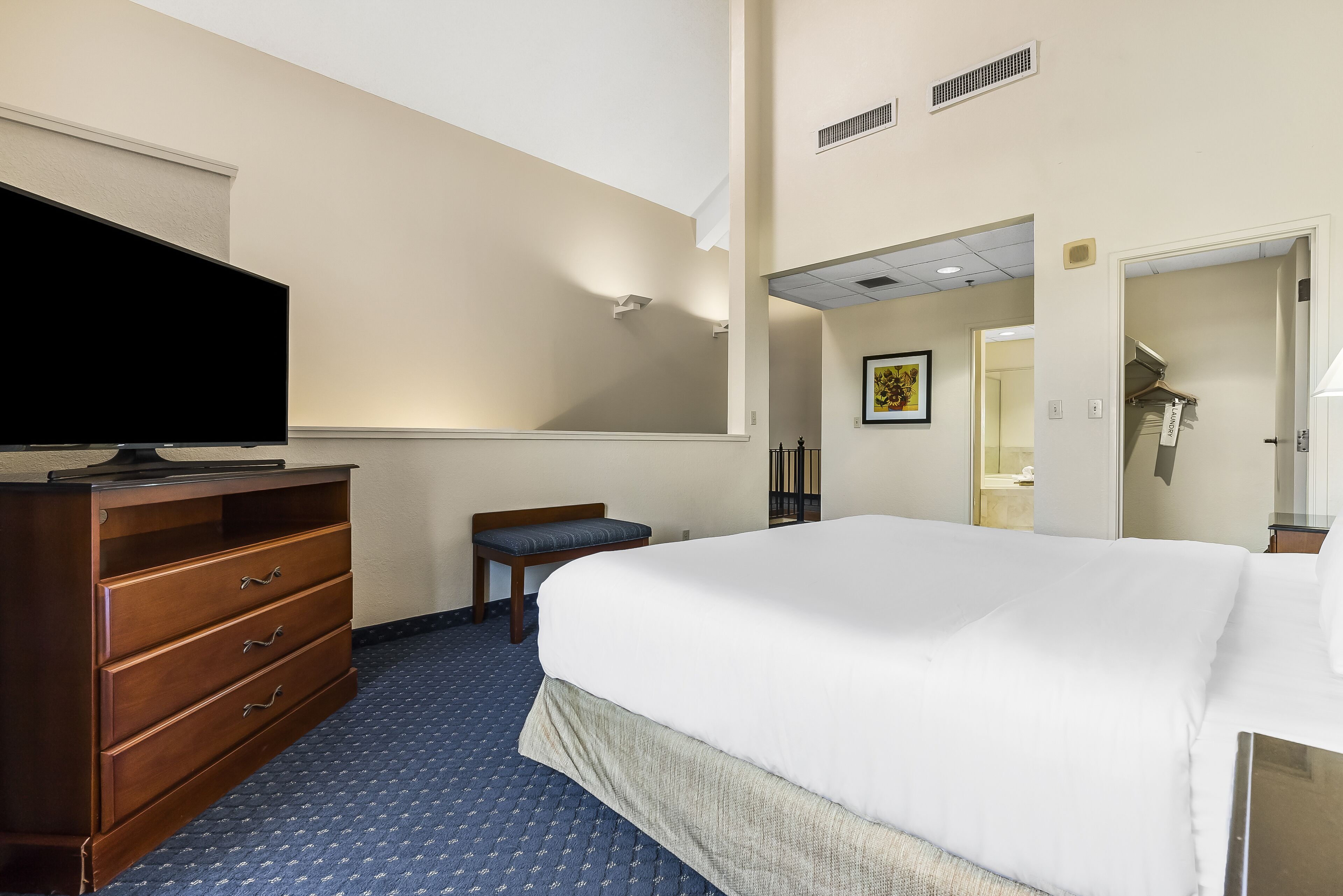 A hotel room with a bed, a dresser, a television, and a bathroom visible through an open door.
