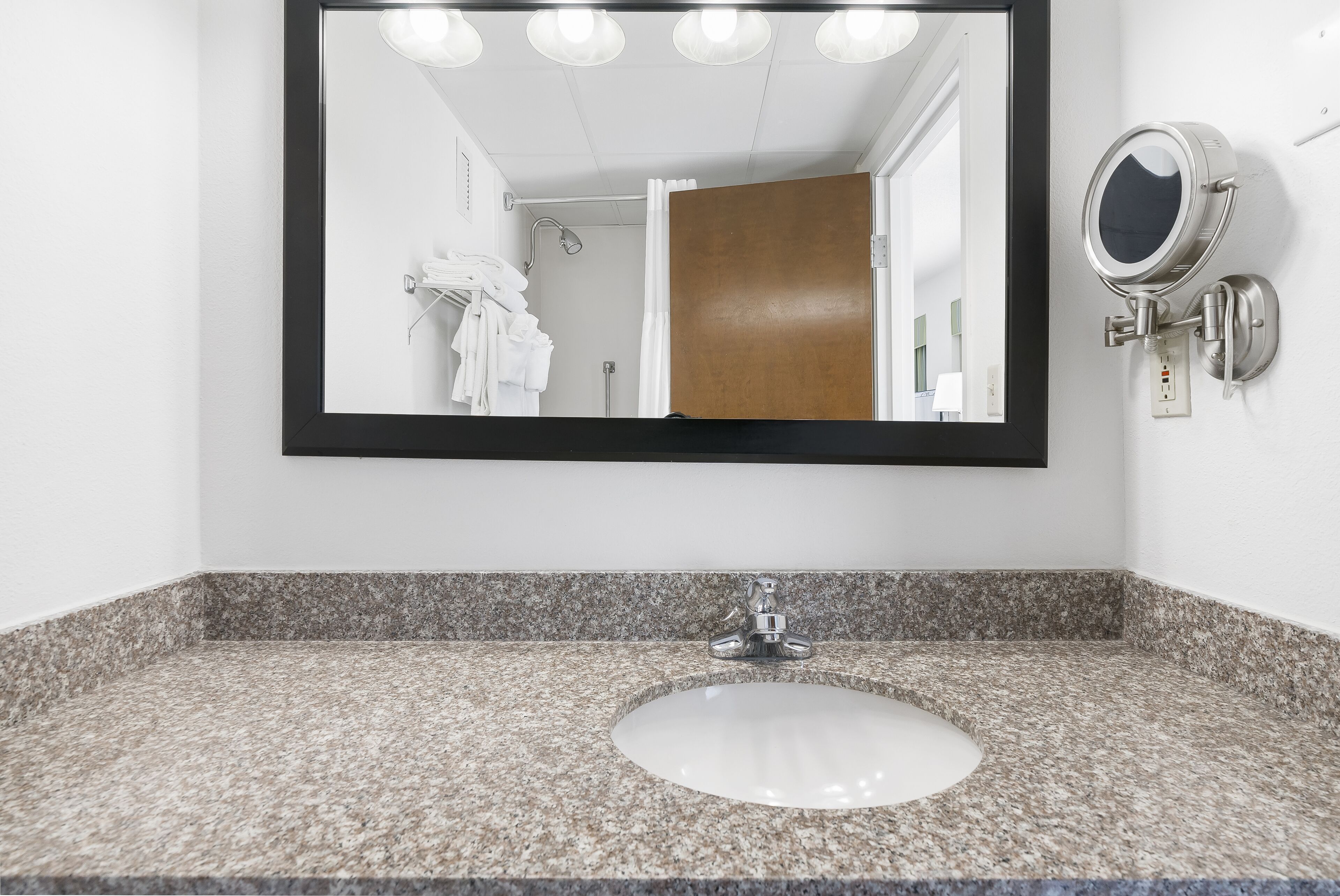 A bathroom with a granite countertop, a white sink, a large mirror, and a wall-mounted vanity light.