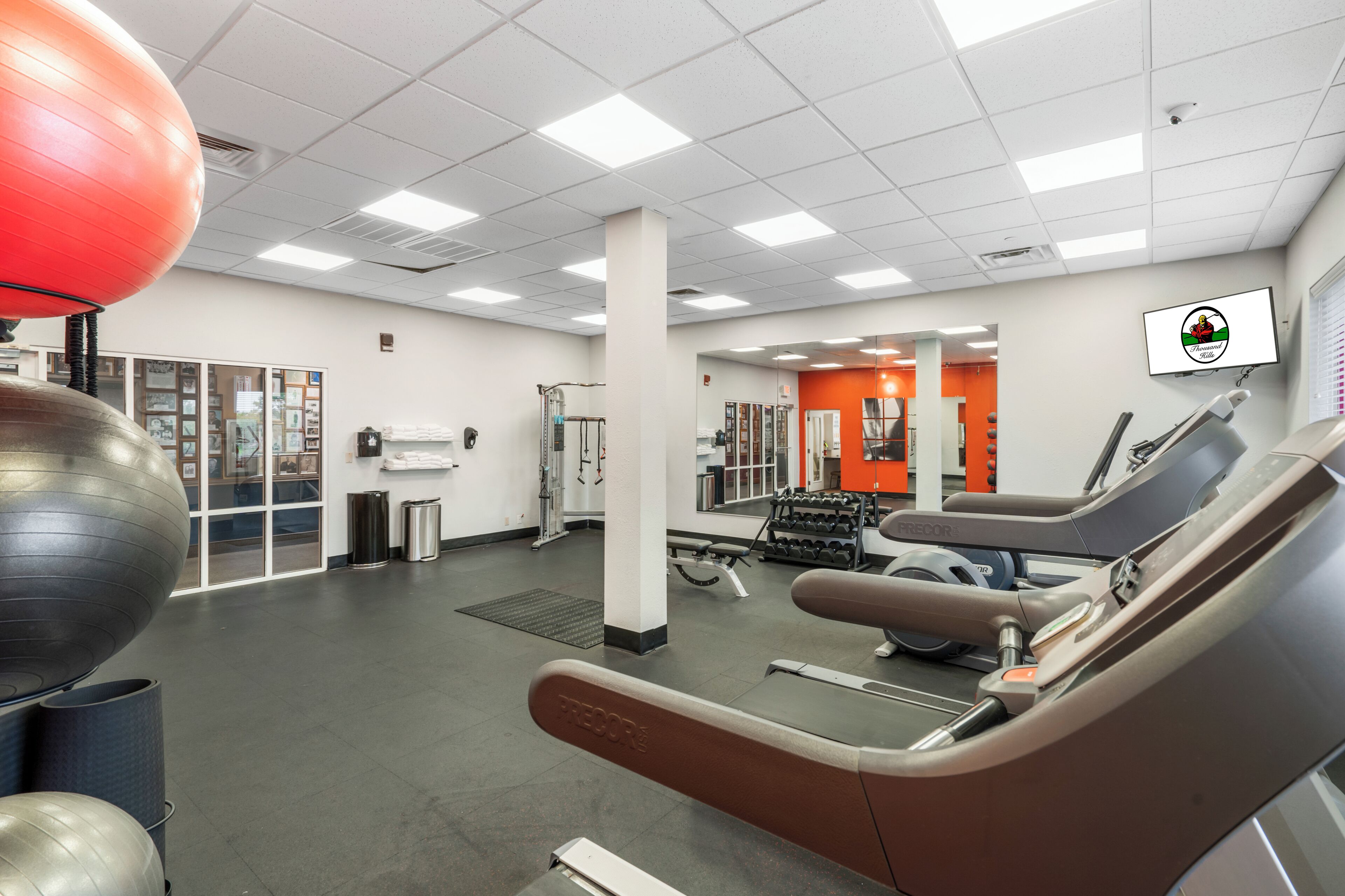 A gym with exercise equipment, a large red exercise ball, and a wall-mounted TV.