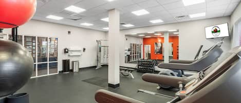 A gym with exercise equipment, a large red exercise ball, and a wall-mounted TV.