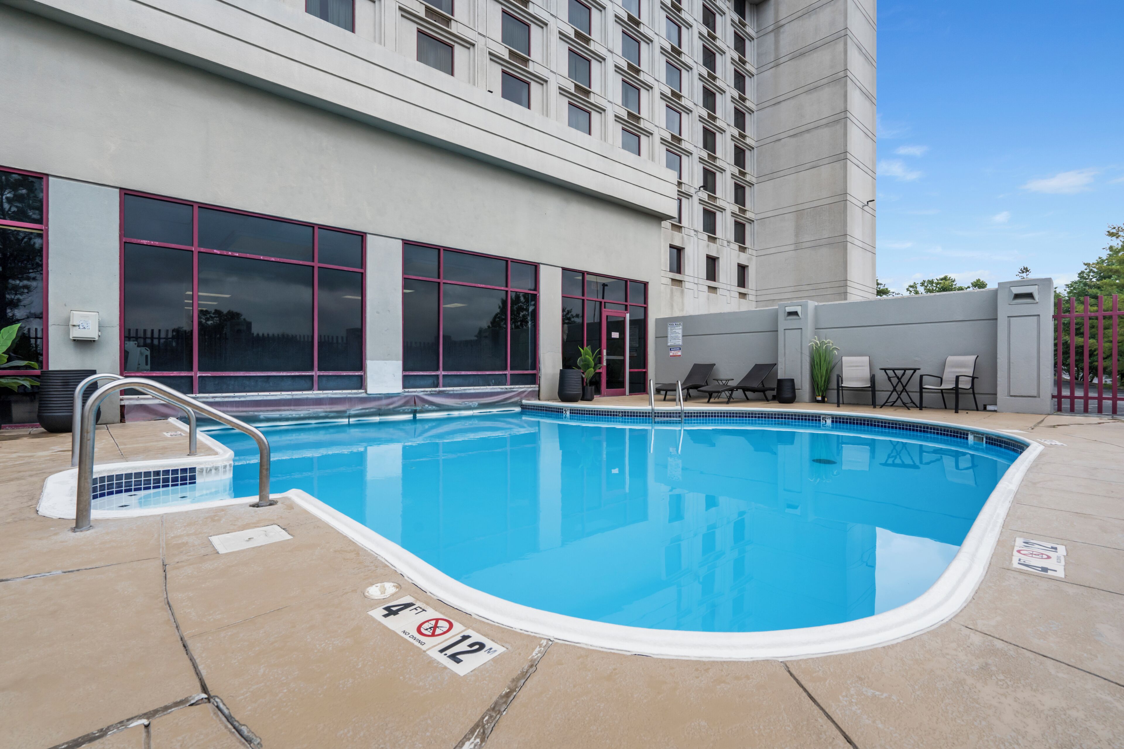 An outdoor swimming pool with a 4ft depth limit, adjacent to a building with large windows and a grey exterior.