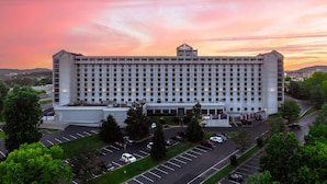 Un hotel grande de varios pisos con una fachada simétrica, una entrada central y un estacionamiento con varios automóviles.