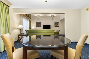 Habitación de hotel con una mesa redonda, dos sillas, un sofá, un televisor y cuadros en la pared.