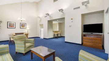 A hotel room with striped armchairs, a small table, a TV, and a blue carpet.