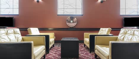 Ein Zimmer mit vier Ledersesseln, einem schwarzen Tisch in der Mitte und einem gemusterten Teppich.