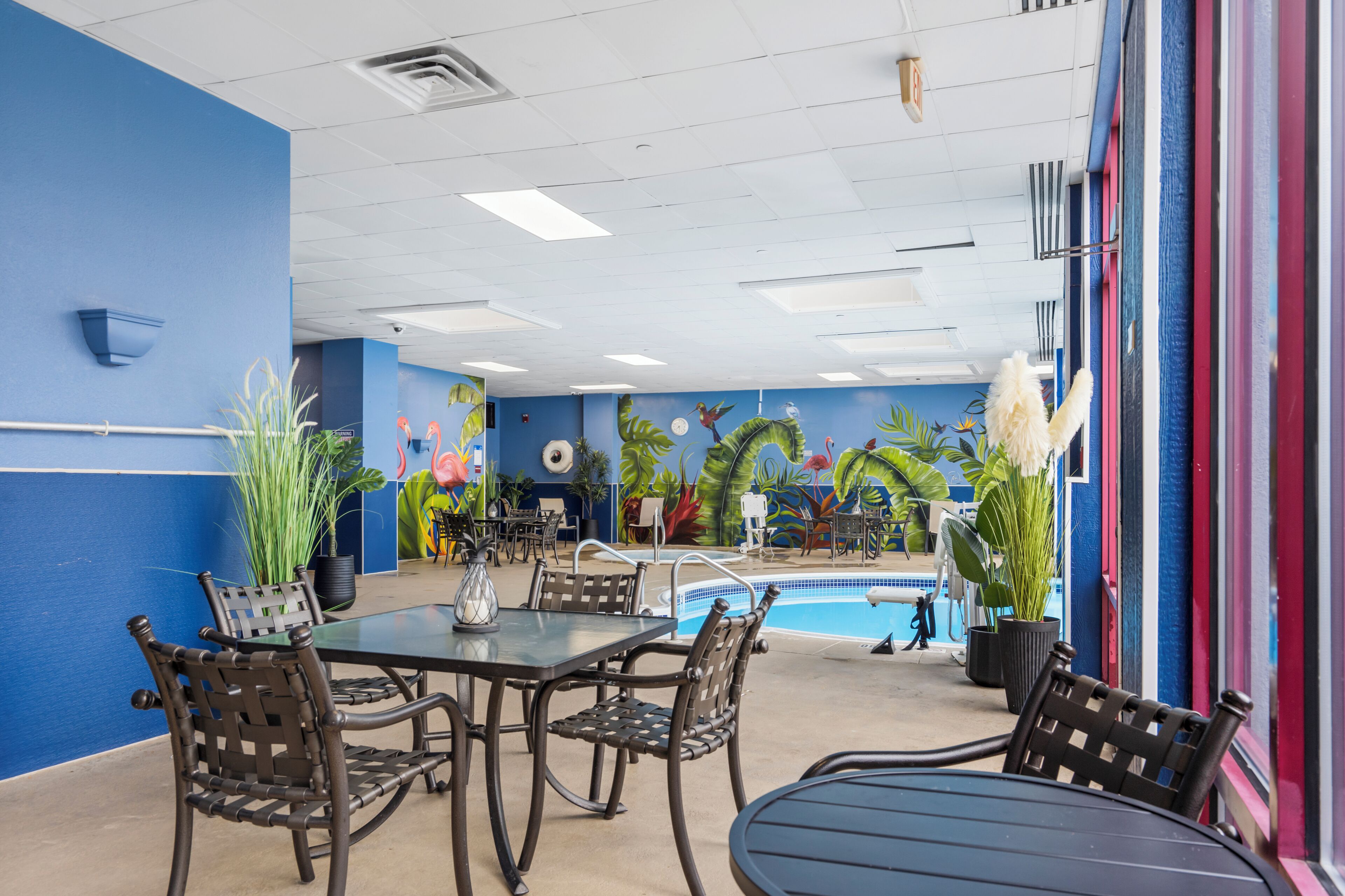 An indoor pool area with a blue wall, a pool table, and several chairs.