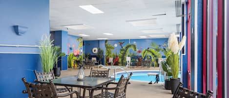 An indoor pool area with a blue wall, a pool table, and several chairs.