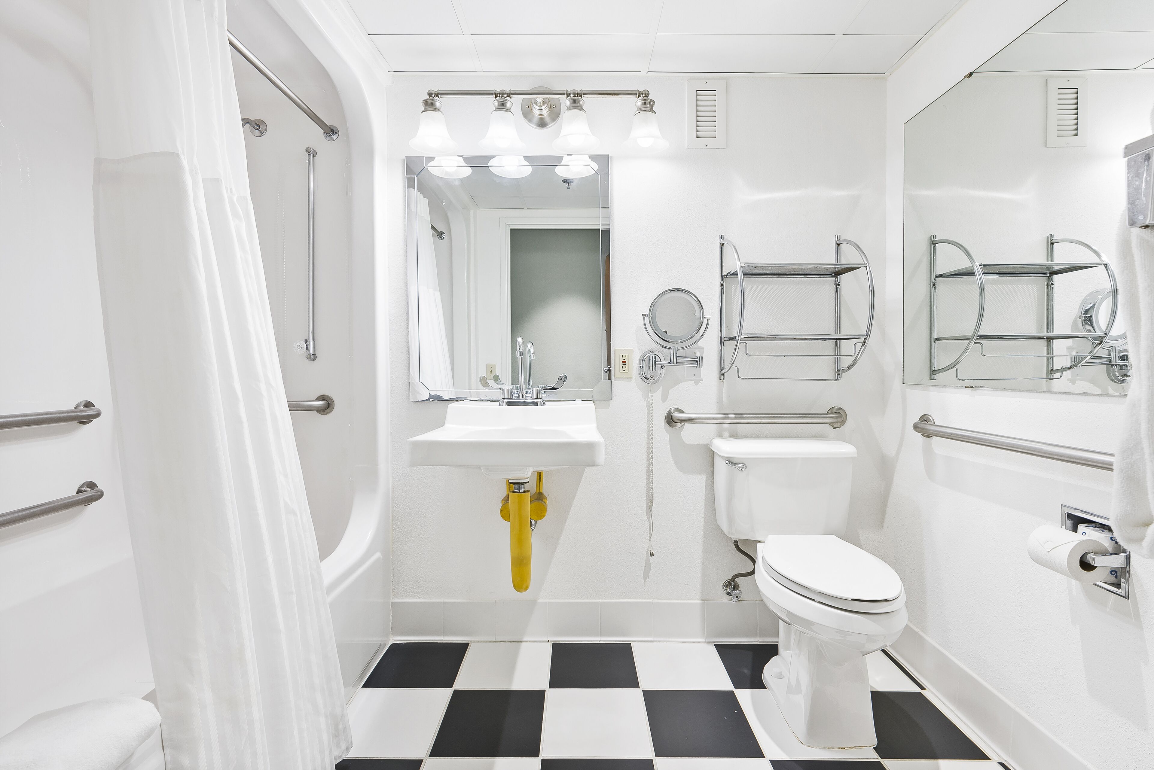 A bathroom with a white sink, toilet, and mirror, a shower area, and a checkered floor.