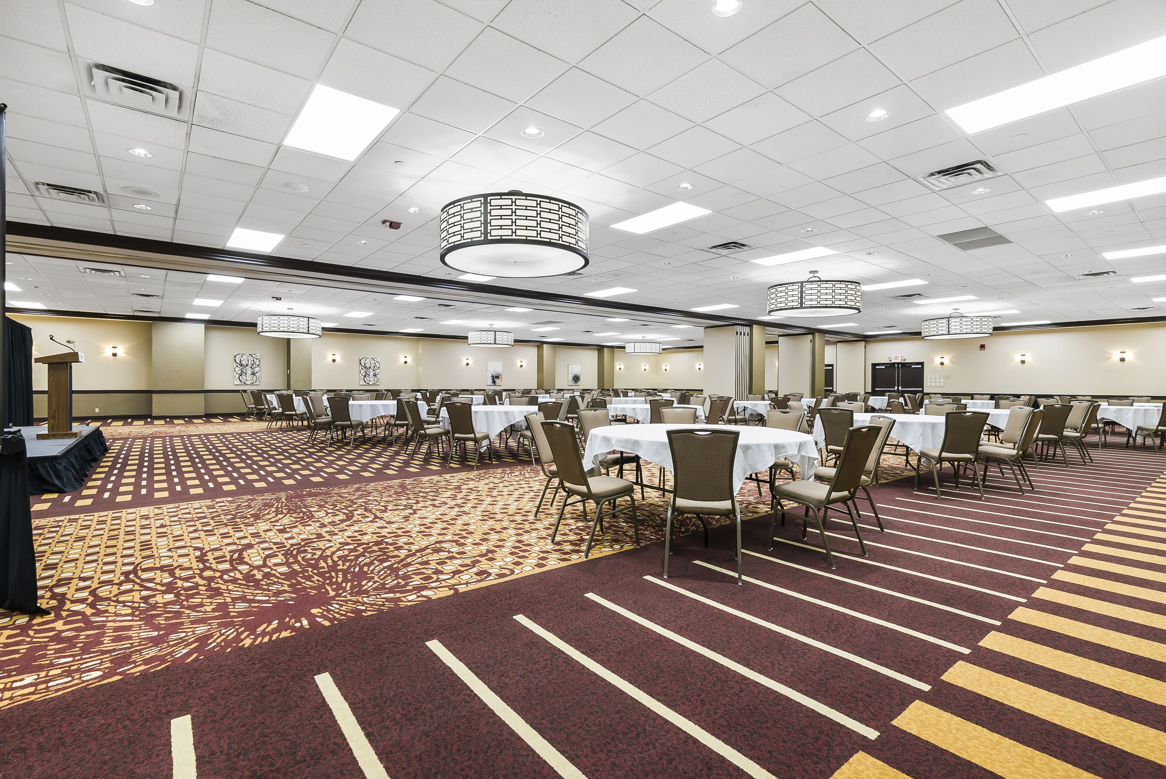 A large conference room with round tables and chairs, a patterned carpet, and a ceiling with recessed lighting.