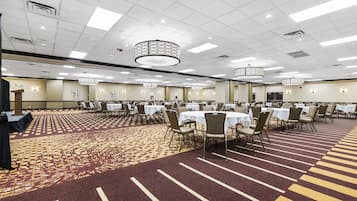 A large conference room with round tables and chairs, a patterned carpet, and a ceiling with recessed lighting.