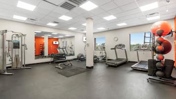 A gym with various exercise equipment, a mirror, a clock, and a window with a view.