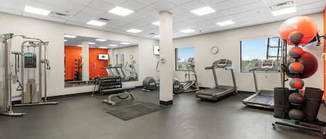 A gym with various exercise equipment, a mirror, a clock, and a window with a view.