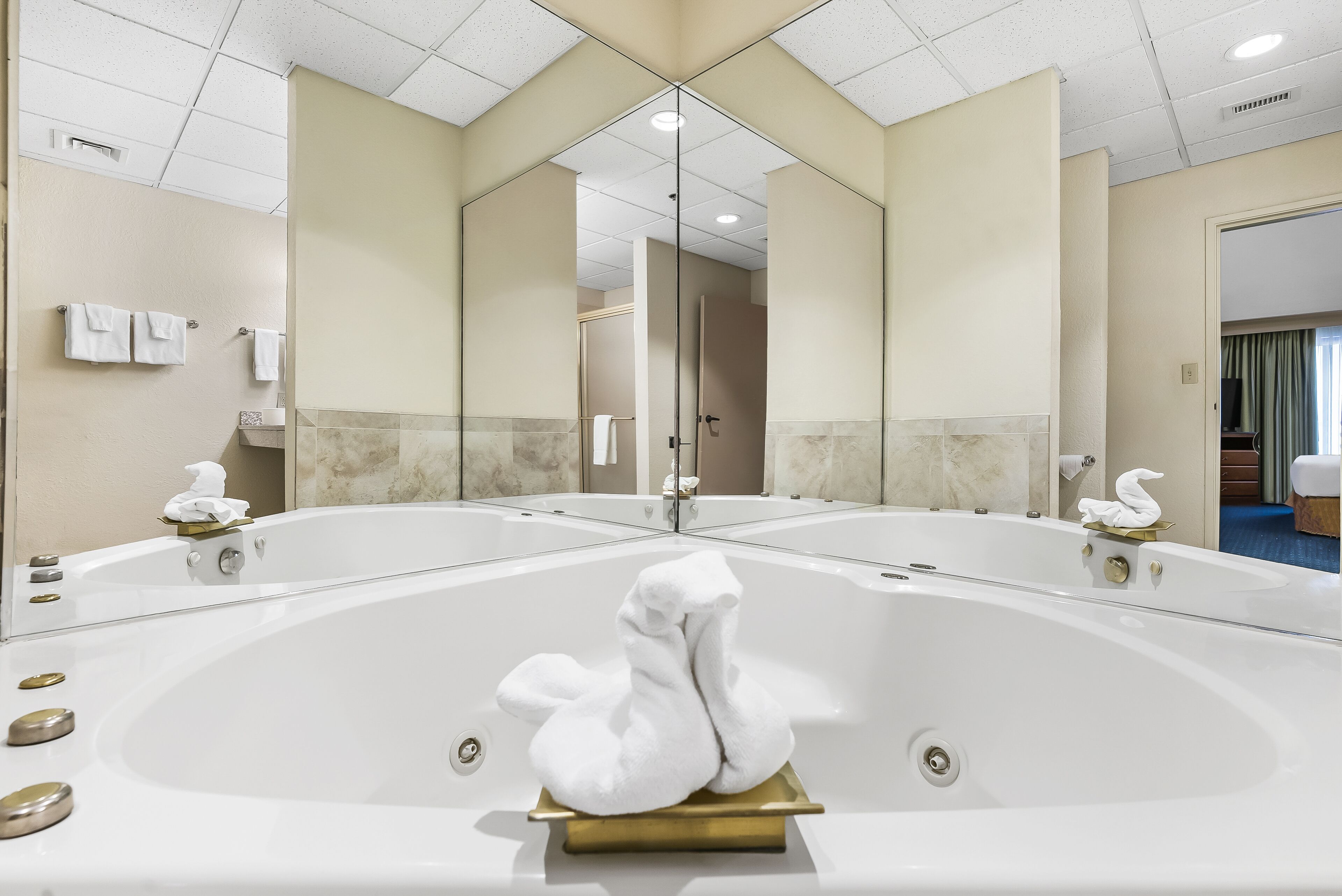 A large, oval-shaped bathtub with a gold base, surrounded by mirrors and beige walls.