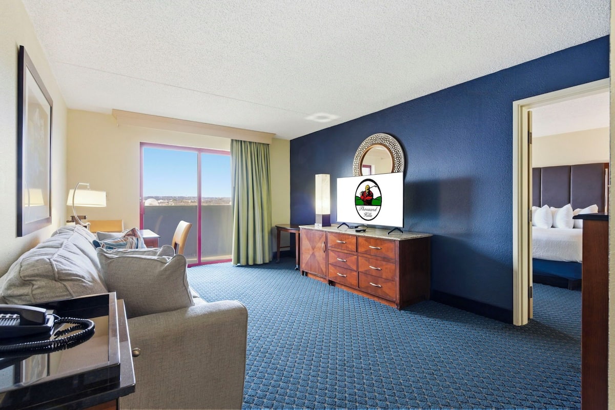 Quarto de hotel com sofá, televisão, cômoda e um espelho grande.
