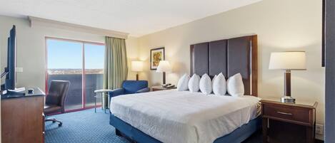 A hotel room with a large bed, a desk, a chair, a TV, and a window with a view.