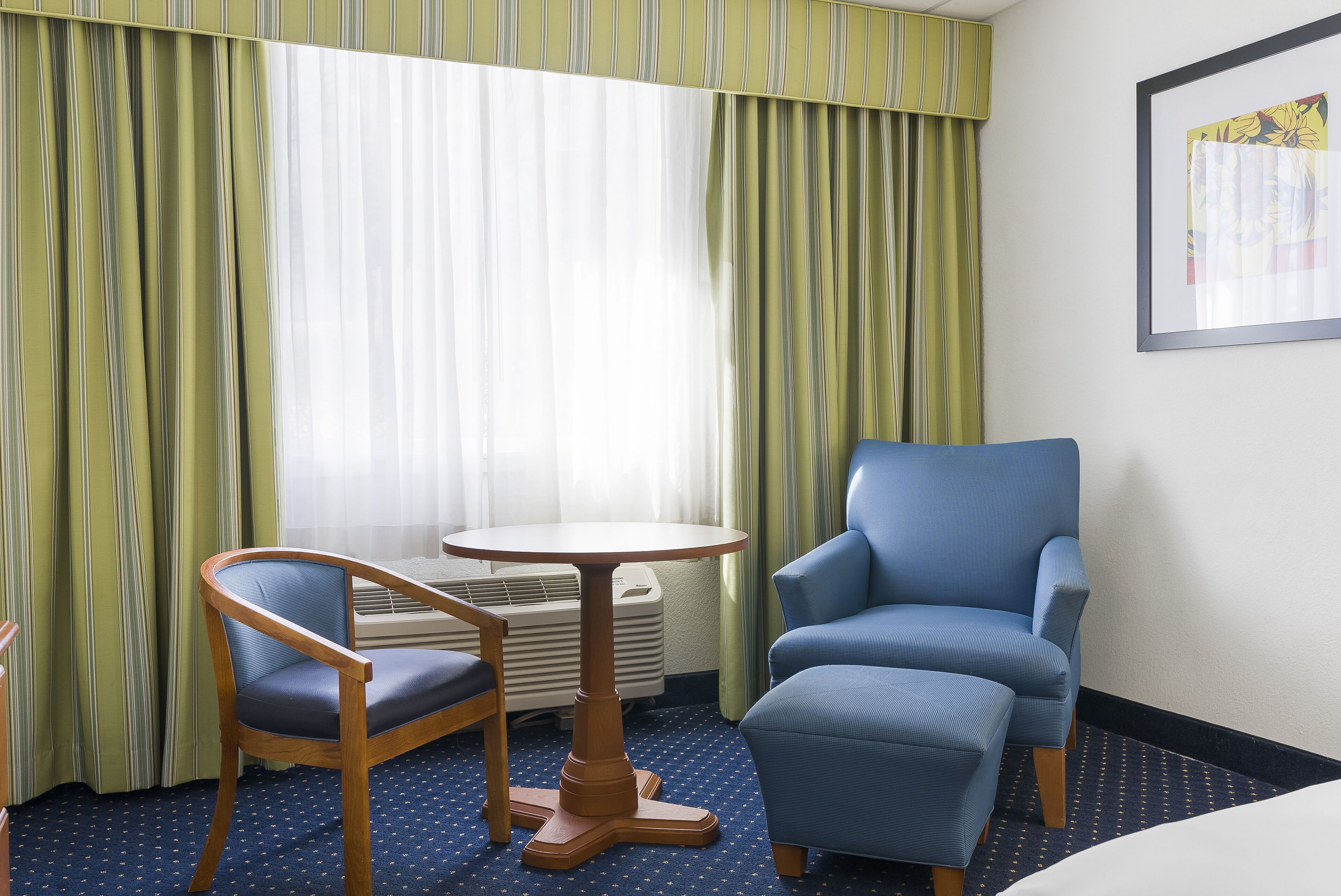 Una habitación de hotel con un sillón azul, una silla de madera y una mesita redonda.