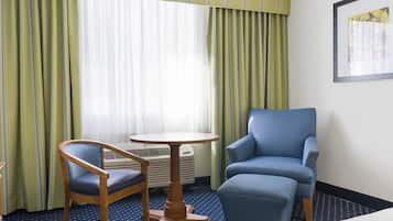 A hotel room with a blue armchair, a wooden chair, and a small round table.