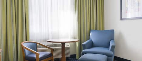 A hotel room with a blue armchair, a wooden chair, and a small round table.
