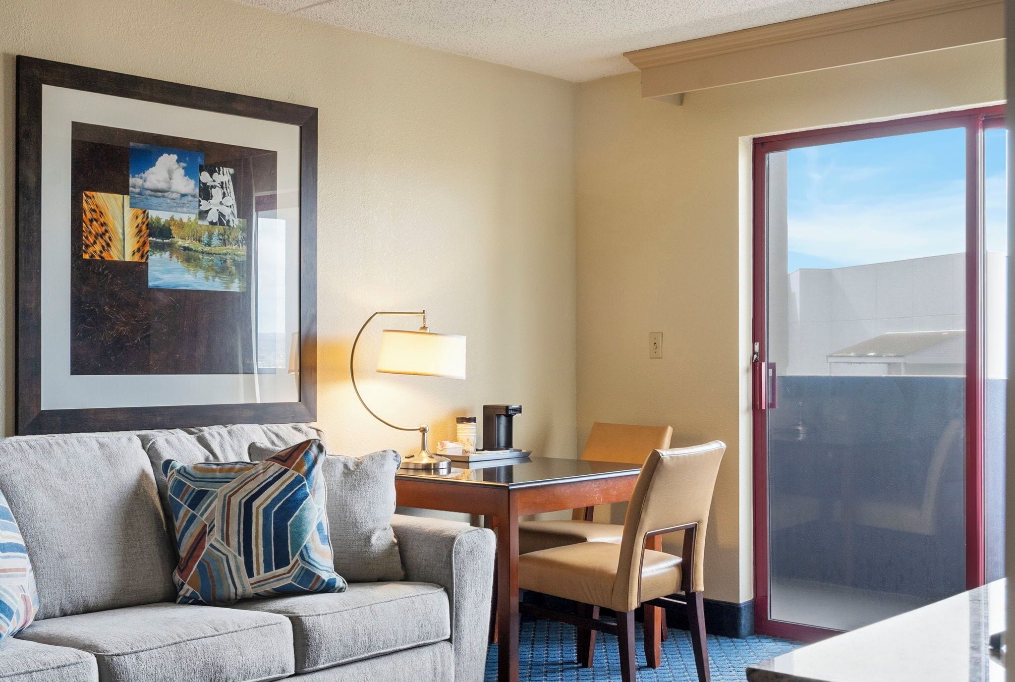 A hotel room with a sofa, a dining table, a lamp, and a framed picture on the wall.