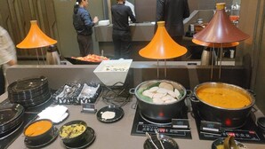 Una mesa de buffet con diversos platos, incluyendo una olla grande de sopa y un tazón de arroz.
