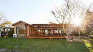 Et hus med overdækket terrasse, græsplæne og et træ.