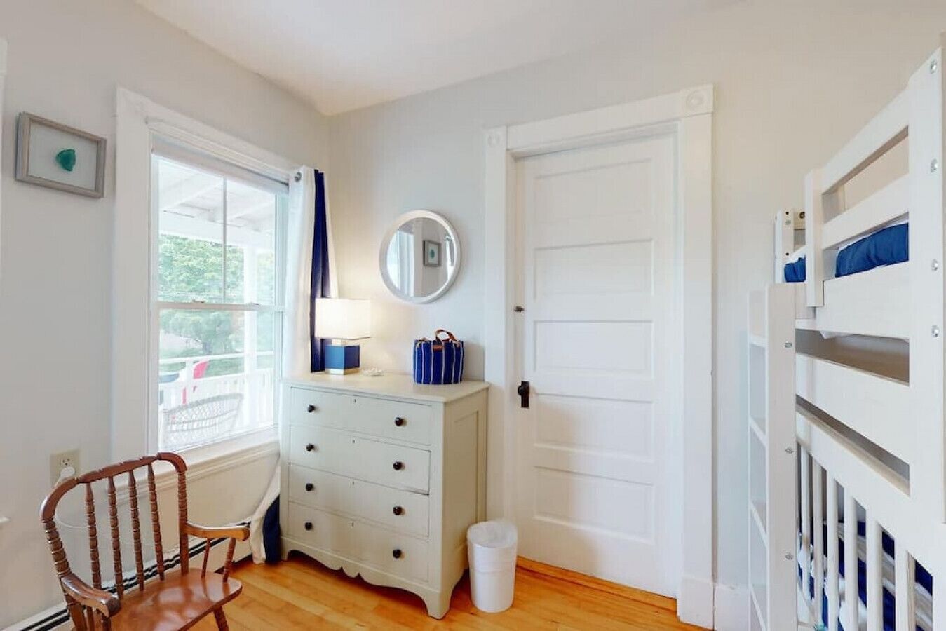 A room with a white dresser, a mirror, a window with curtains, a door, and a bunk bed.