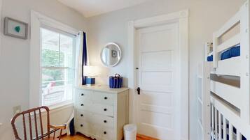A room with a white dresser, a mirror, a window with curtains, a door, and a bunk bed.