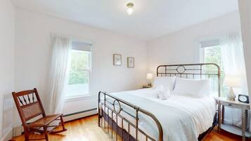 A bedroom with a metal bed frame, white bedding, a wooden rocking chair, and two bedside tables with lamps.