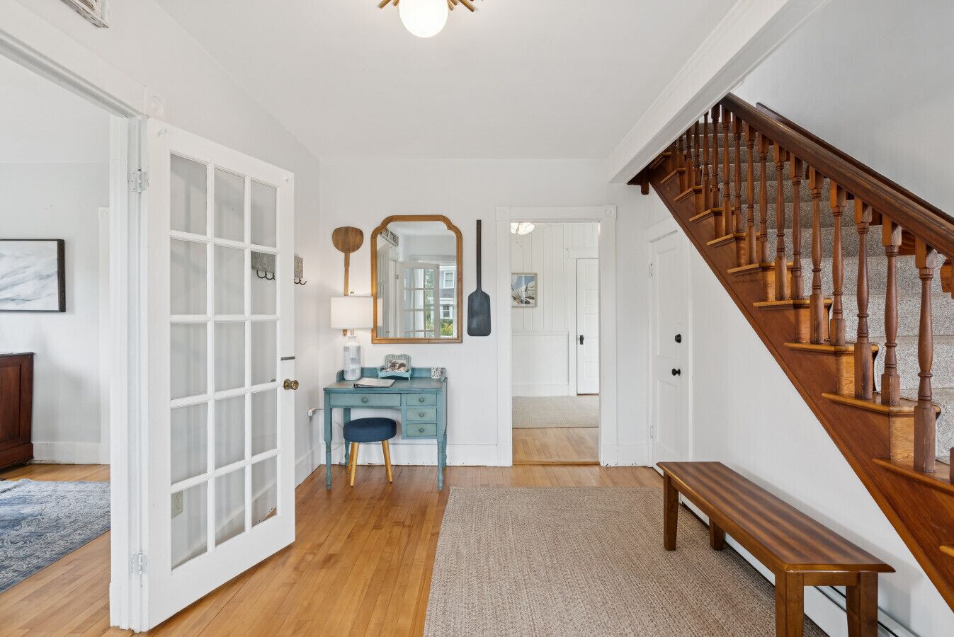 A hallway with a wooden staircase, a blue vanity with a mirror, and a bench.