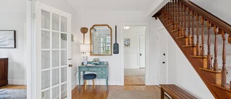 A hallway with a wooden staircase, a blue vanity with a mirror, and a bench.