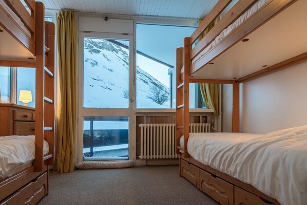 Una habitación con literas, una ventana con vista a una montaña nevada y un radiador.