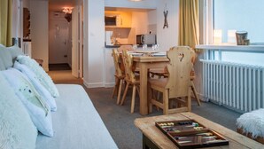 A cozy living room with a sofa, a dining table with chairs, a wooden coffee table, and a view of a kitchen and a window with curtains. - In the center of town, close to the ski slopes, 3 rooms, 2 bedrooms for 4 people (Val-d'Isère)