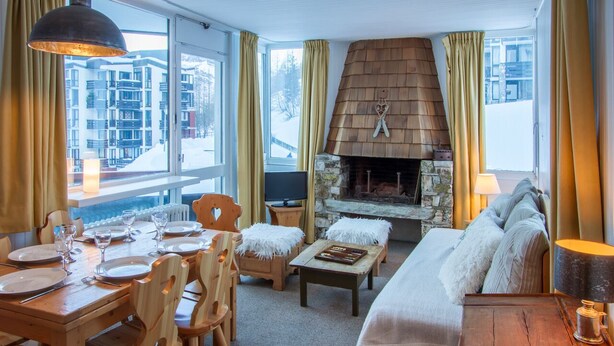 A cozy room with a stone fireplace, wooden furniture, and large windows offering a view of a snowy landscape. - In the center of town, close to the ski slopes, 3 rooms, 2 bedrooms for 4 people (Val-d'Isère)