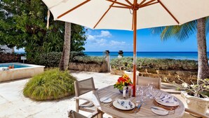 An outdoor dining area with a table set for four, surrounded by chairs, under a large umbrella. - Enchanting Beachfront Retreat - Leamington Cottage 1 Bedroom Villa by Blue Sky Luxury (Speightstown)