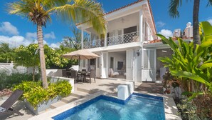 A two-story house with a swimming pool, outdoor furniture, and lush greenery.